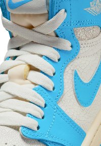 Sneaker alta con pelle bianca screpolata, dettagli blu vivaci e lacci bianchi. Presenta un grande Swoosh blu e un design texture.