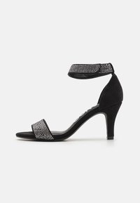 Sandalo con tacco alto in suede nero, con cinturino alla caviglia e fascia sul davanti decorati con strass, che presenta un design del tacco affusolato.
