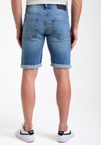Lichtblauwe denim shorts met opgerolde mouwen, twee achterzakken en een donkerleren label op de tailleband; gedragen met witte Nike sneakers.