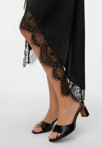 Melna satīna svārki ar mežģīņu apdari un ziedu rakstiem. Melnas sandales ar atvērtām purngalu daļām un bieza papēža blokiem papildina izskatu.