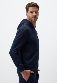 Felpa blu navy realizzata in materiale morbido, con tasca anteriore e cappuccio regolabile con cordino, maniche lunghe e vestibilità comoda.