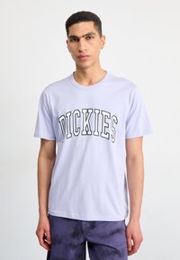 Levandulové bavlněné tričko s zakřiveným černým potiskem loga "DICKIES" na hrudi. Krátké rukávy a kulatý výstřih.