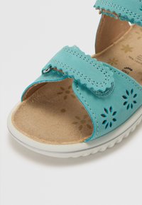 Turkos sandal med perforerat blommönster, justerbart rem och strukturerad innersula. Gummisula har ett vågmönster för grepp.