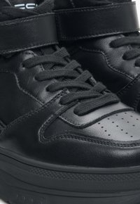 Czarne skórzane sneakersy z wysoką cholewką, płaskimi sznurowadłami, perforowaną strefą palców oraz szerokim paskiem na rzepie wokół kostki.