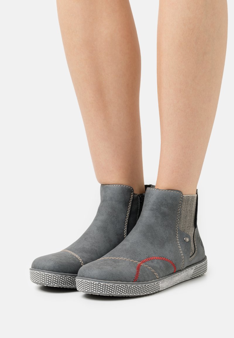 Bottines en suède gris avec panneaux latéraux élastiques, surpiqûres rouges contrastantes et semelle en caoutchouc blanc texturé.