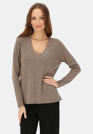 Brązowy, długi sweter z długim rękawem i głębokim dekoltem w serek, wykonany z miękkiego materiału, o luźnym kroju i subtelnej fakturze, zestawiony z czarnymi spodniami.