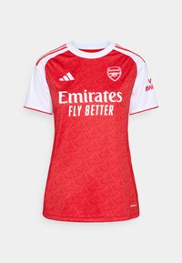 Maillot de football rouge et blanc avec un design à motifs, col rond, manches courtes et logo "Emirates Fly Better" à l'avant.