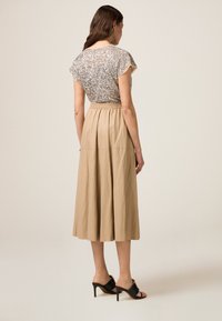 Zilveren, met pailletten bedekte top met cap sleeves, gecombineerd met een beige, vloeiende, enkellange rok met een elastische waistband en een gestructureerde afwerking.