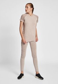 Jasnobeżowy zestaw sportowy składający się z topu z krótkim rękawem z dzianinowymi detalami na ramionach oraz dopasowanych legginsów, wykonanych z przewiewnego materiału.