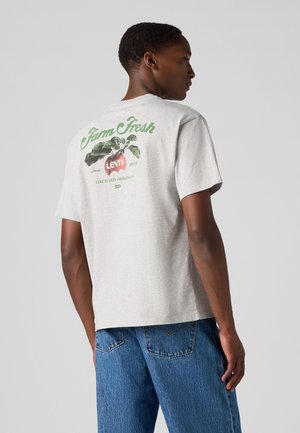 T-shirt grigia in cotone con maniche corte, caratterizzata da testo grafico verde e rosso e un'illustrazione di mela sul retro. Vestibilità casual, texture morbida.