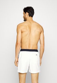 Shorts da bagno bianchi con elastico blu navy in vita, dotati di due tasche laterali e semplici dettagli decorativi. Modello visto da dietro.