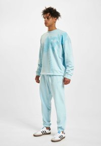 Light blue sweatshirt with palm tree design, paired with matching light blue joggers. Features relaxed fit, ribbed cuffs, and white sneakers.