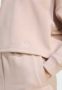 Light pink sweatshirt made of soft fabric, featuring a small white embroidered logo at the hem and a relaxed design with visible seams.