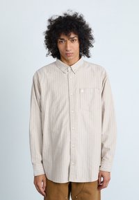 Beige langærmet skjorte med knapper og hvide lodrette striber, krave, brystlomme og knappede manchetter. Glat stof med en afslappet pasform.
