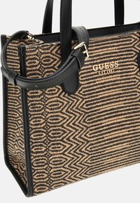 Bruine en zwarte tas met een gestructureerd ontwerp, faux leren accenten en een gouden "GUESS" logo aan de voorkant.