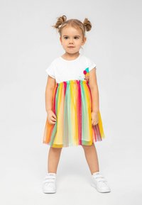 Weißes Kurzarmkleid mit buntem, gestreiftem Tüllrock, verziert mit einem Eisbecherdesign und dem Schriftzug "mein Favorit". Kombiniert mit weißen Sneakern.