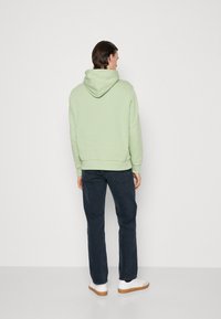Sudadera con capucha verde claro de textura, combinada con jeans oscuros. El modelo lleva zapatillas blancas con suela marrón.
