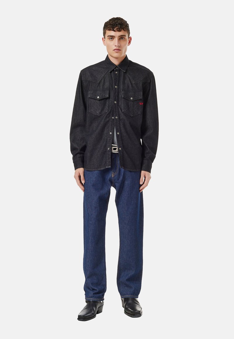 Schwarzes Denim-Hemd mit zwei Brusttaschen, Druckknöpfen und spitzen Kragen, kombiniert mit blauen geraden Jeans und schwarzen Lederstiefeln.