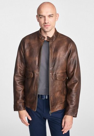 Brązowa skórzana kurtka z kołnierzem stójkowym, zapięciem na zamek, dwoma przednimi kieszeniami i ściągaczami na mankietach. Gładka faktura z subtelnymi oznakami starzenia.