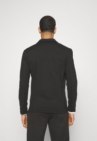 Sort langærmet skjorte med krave, lavet af et glat stof. Har en lige skæring og minimalistisk design.