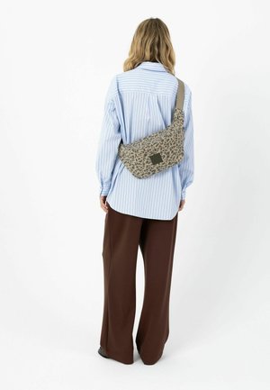 Persona vistiendo pantalones marrones sueltos y una camisa azul claro a rayas, llevando una bolsa cruzada beige con estampado de leopardo en la espalda.