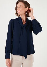 Marineblouse met een gestrikt striknek, lange mouwen en knoopdetails bij de manchetten, gemaakt van een gladde, lichtgewicht stof.