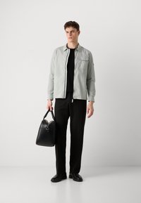 Ανοιχτό γκρι, υφασμάτινο πουκάμισο τοποθετημένο πάνω από ένα μαύρο μπλουζάκι, συνδυασμένο με μαύρο παντελόνι. Μαύρη δερμάτινη τσάντα με στρογγυλό σχήμα κρατιέται στο ένα χέρι.