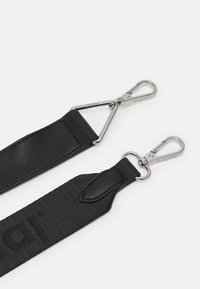 Schwarzer Riemen mit zwei Befestigungsclips; eine Seite ist aus glattem Leder, die andere hat ein strukturiertes Gewebe mit einem Logo. Silberne Hardware-Akzente.