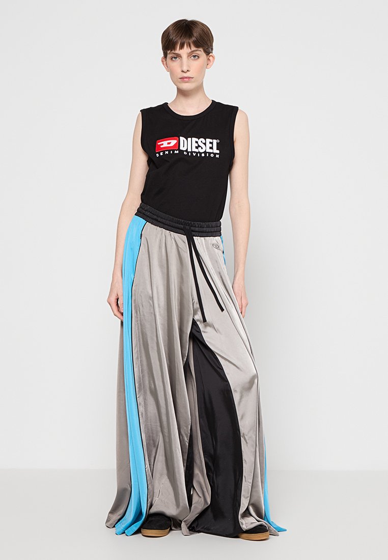 Haut sans manches noir avec le logo "DIESEL" blanc, associé à un pantalon large en satin multicolore avec des panneaux gris, bleu et noir.