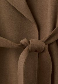 Brązowy, miękki płaszcz z tkaniny o kopertowym kroju i paskiem wiązanym w talii. Faktura wydaje się ciepła i puszysta.