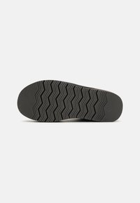 Shoe sole featuring a textured dark gray rubber surface with a zigzag pattern for traction and a rounded toe.