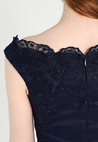 Navy dress with floral lace detailing along the scalloped neckline and back, featuring a zipper closure and smooth, textured fabric.