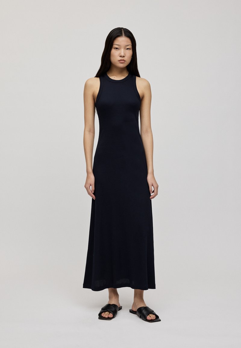 Abito maxi senza maniche di colore navy con un corpetto aderente, texture liscia e una lunga gonna fluente. Abbinato a sandali flat neri.