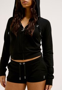 Schwarze, verkürzte Zip-Hoodie mit Kordelzug, kombiniert mit schwarzen Shorts mit elastischem Bund und silbernen Hardware-Akzenten.