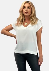 Biała bluzka z krótkim rękawem i dekoltem w kształcie litery V, wykonana z lekkiego, gładkiego materiału. Posiada luźny krój i lekko zakrzywiony dół.