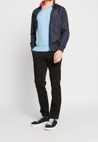 Marineblaue Bomberjacke mit rotem Futter, hellblaues V-Ausschnitt-Pullover, schwarze Hose und marineblaue Sneaker mit weißen Sohlen.
