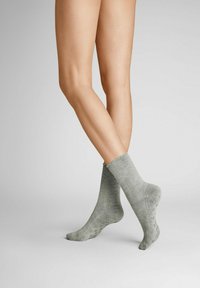 Graue Knöchelsocken mit einem gerippten Muster, ausgestattet mit einem gewellten Saum und einem weichen, leichten Material, auf nackten Beinen vor einem neutralen Hintergrund präsentiert.