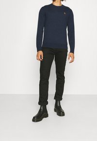 Navy-Strickpullover mit Rundhalsausschnitt, kombiniert mit schwarzen, schmal geschnittenen Hosen und schwarzen Stiefeletten mit dicker Sohle.