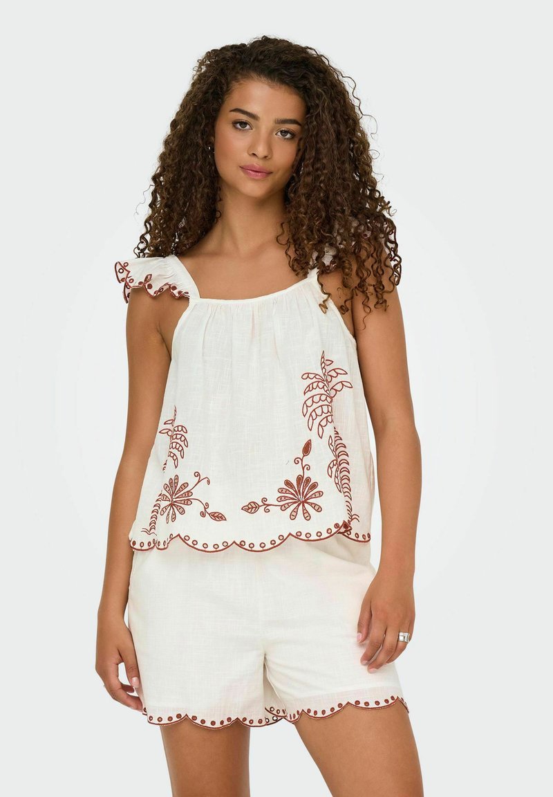 Top bianco ricamato con spalline a volant, caratterizzato da motivi floreali rossi e orlo scalloppato, abbinato a pantaloncini bianchi coordinati.