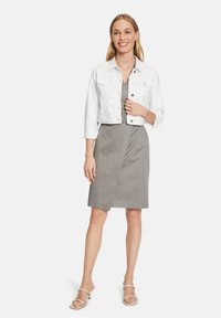 Witte cropped denimjacket over een grijze wikkeljurk, aangevuld met neutrale block-heeled sandalen. Vloeibare stof en getailleerd ontwerp.