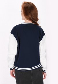 Pulover bleumarin cu alb, cu mâneci raglan, manșete și tiv cu textură mată și un contrast de culori.