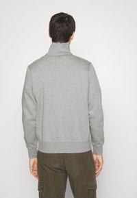 Gray sweatshirt with a high collar and ribbed cuffs. Material has a soft texture. Seen from the back, worn with olive cargo pants.