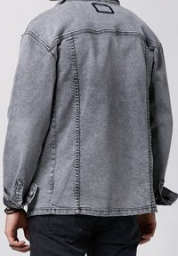 Denim takki, joka on pesty harmaan väriseksi ja siinä on rento istuvuus. Takissa on nepparikiinnitys, säädettävät hihansuut ja takana selkäpaneelin yksityiskohtia.