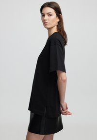 Zwarte oversized t-shirt met korte mouwen, met zijsplitten aan de zoom, gemaakt van zachte katoenen stof, gecombineerd met een zwarte leren mini rok.