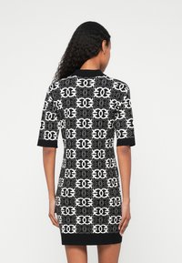 Vestido de malha com um padrão geométrico em preto e branco, mangas curtas e uma silhueta ajustada, com um decote e acabamentos inferiores em preto sólido.