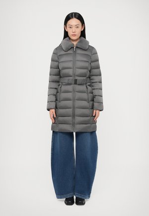 Abrigo acolchado gris con cuello de piel, cintura ajustada, mangas largas y cierre delantero con cremallera; combinado con pantalones vaqueros de pierna ancha y zapatos negros.