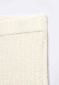 Tissu côtelé crème avec une texture douce et un poignet replié. La surface présente de subtiles rayures verticales.