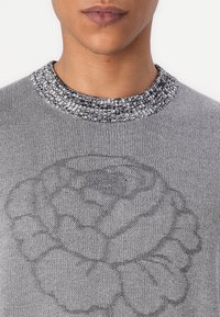Gray knit sweater featuring a floral pattern in a darker shade, with a textured black-and-white ribbed neckline.