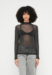 Top nero trasparente a maniche lunghe con riflessi metallici, abbinato a un reggiseno coordinato; completato con jeans in denim grigio a vita alta.