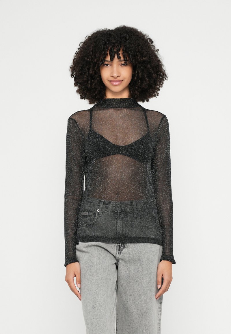 Top nero trasparente a maniche lunghe con riflessi metallici, abbinato a un reggiseno coordinato; completato con jeans in denim grigio a vita alta.